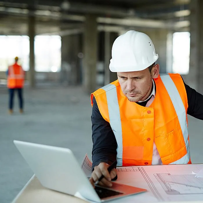 Construction professional using a laptop beside project drawings on site